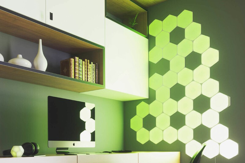 Nanoleaf Shapes Hexagon LED lights shining green next to a computer on a wall. 