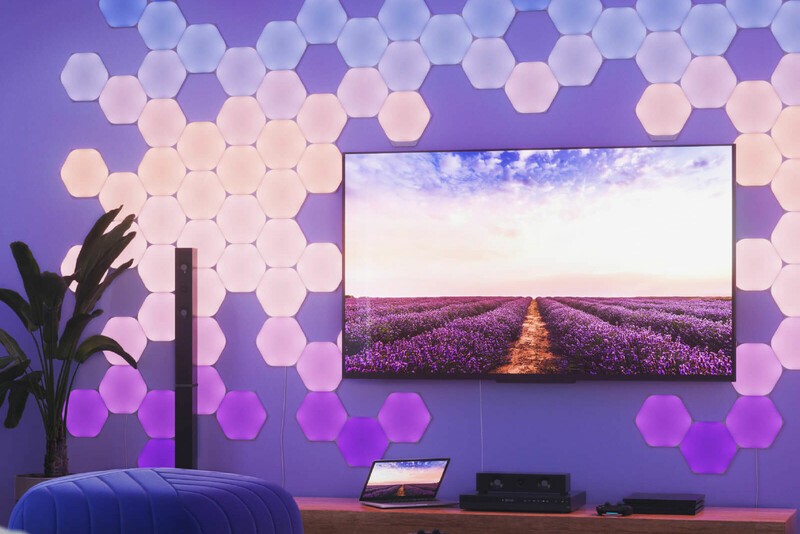 Nanoleaf Shapes Hexagon LED lights shining pink and purple beside a TV from the wall behind it. 