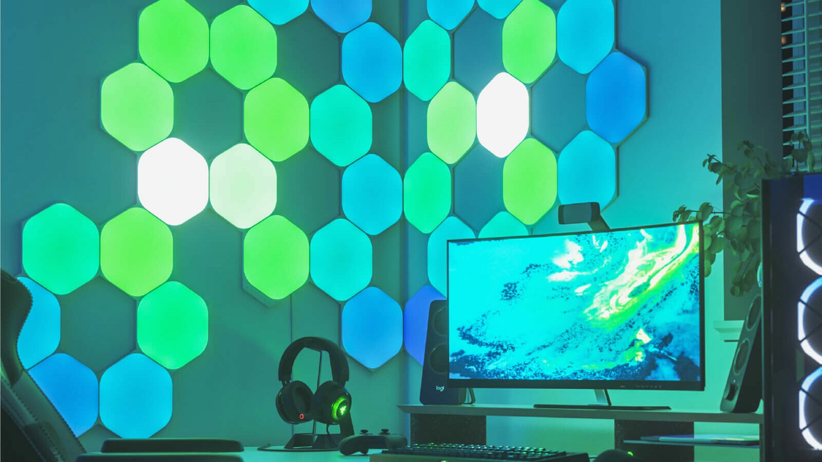 Nanoleaf Shapes Hexagon LED lights shining green in next to a computer on a wall. 